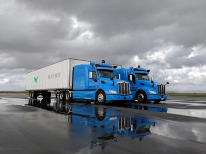 Two, blue Waymo Via trucks on a rainy tarmac 