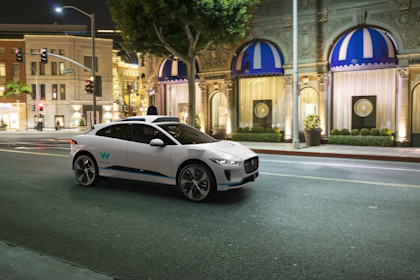 A rendering of a white, I-PACE with the 4th-generation Waymo Driver in an urban setting
