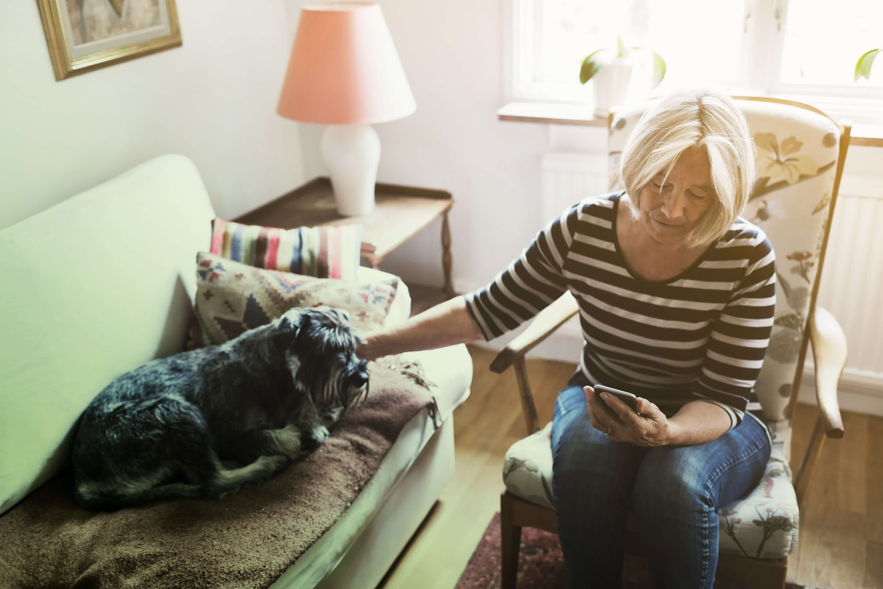 En kvinna sitter hemma med hund och tittar på sin mobil.