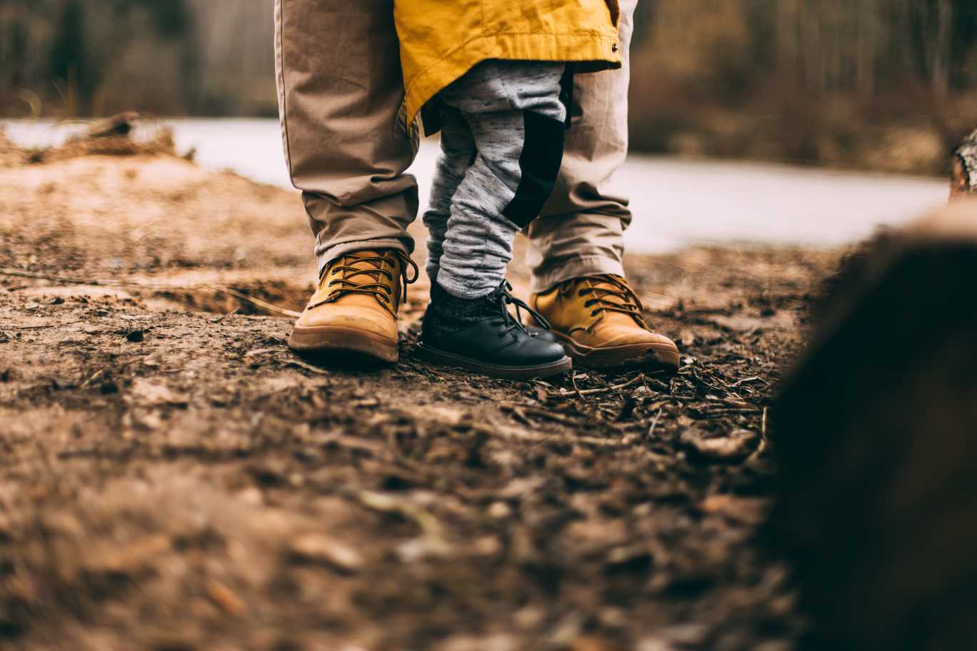 En vuxen och ett barn, deras fötter på grusig mark. Fotograf: Daiga Ellaby