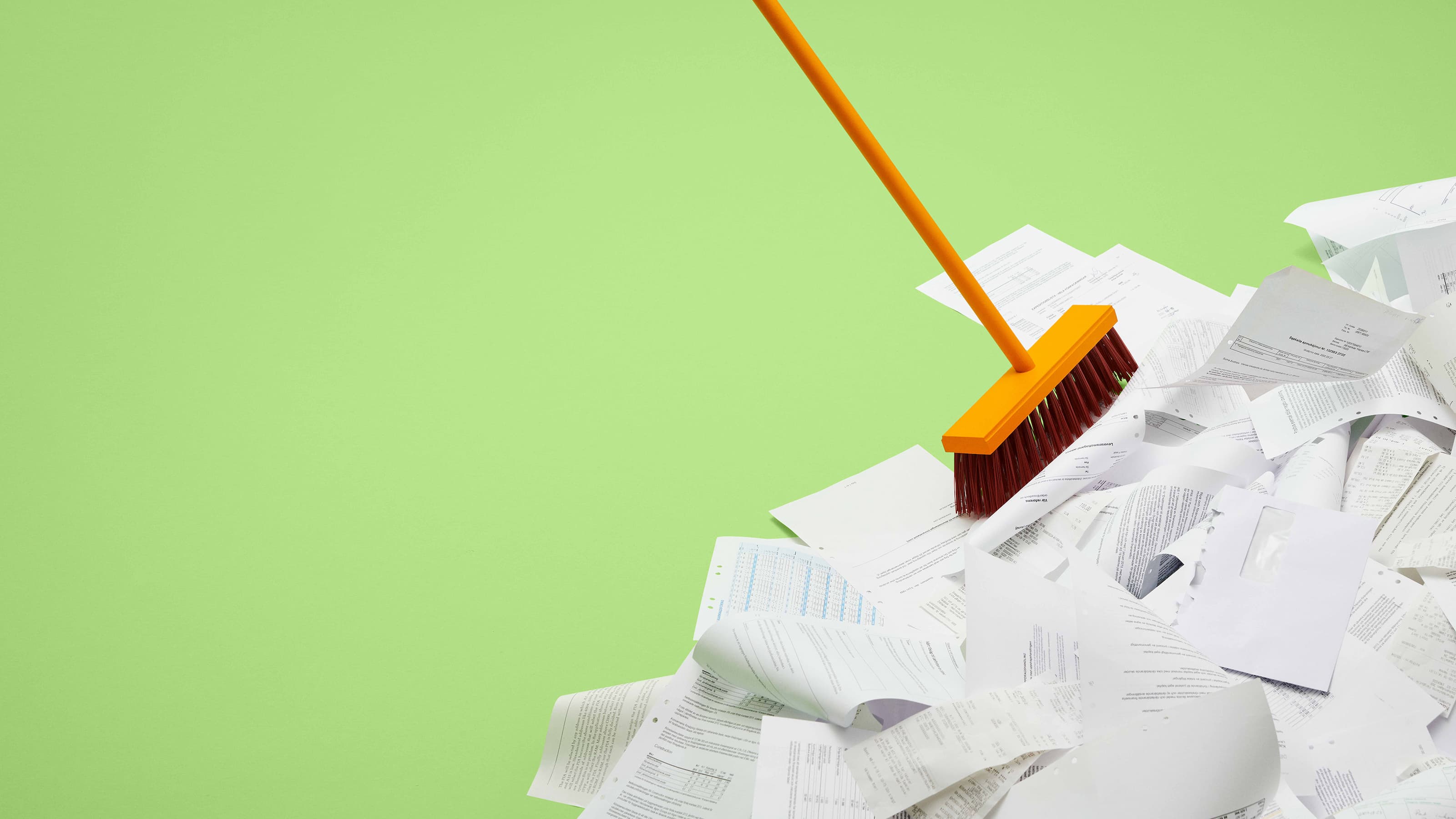 A broom brushes away a messy pile of paper documents.