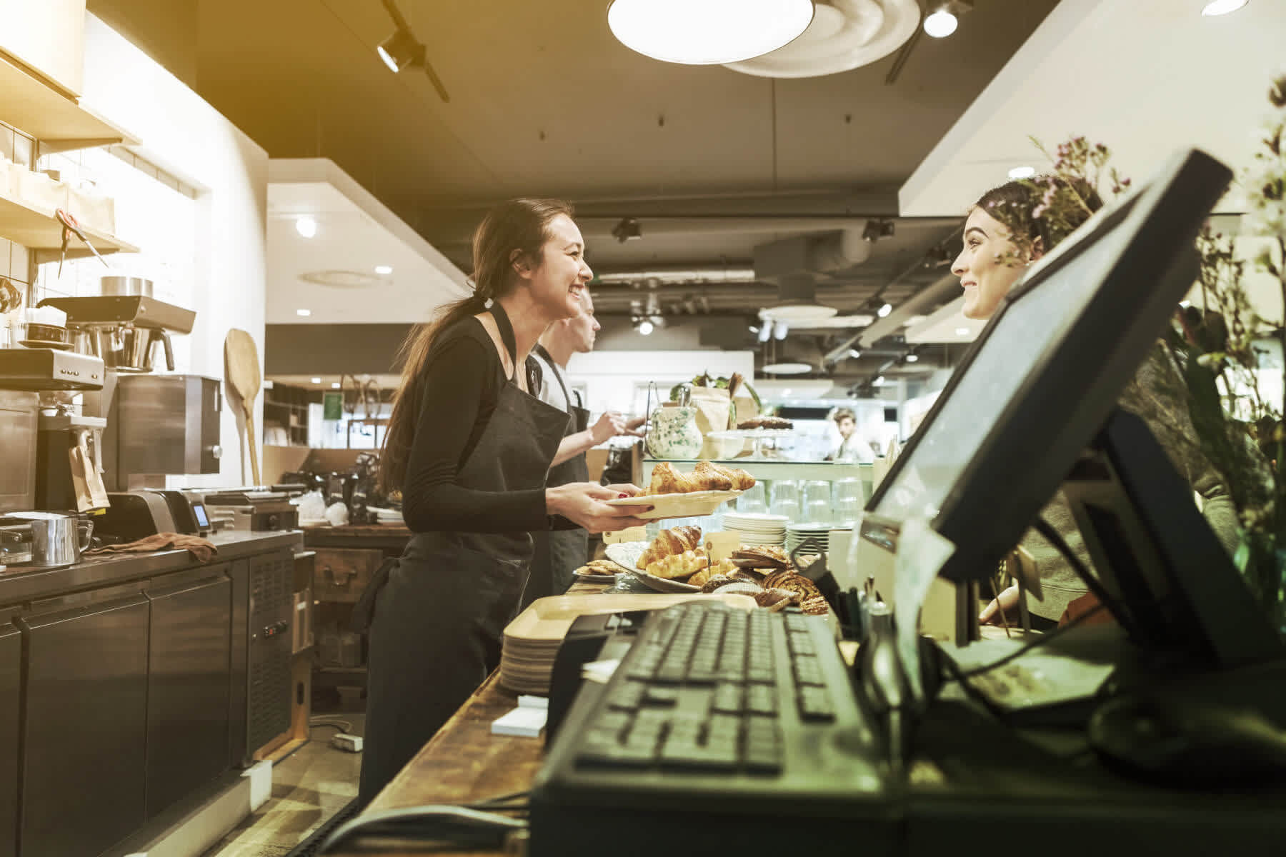 Two women talking over an order counter at a café.