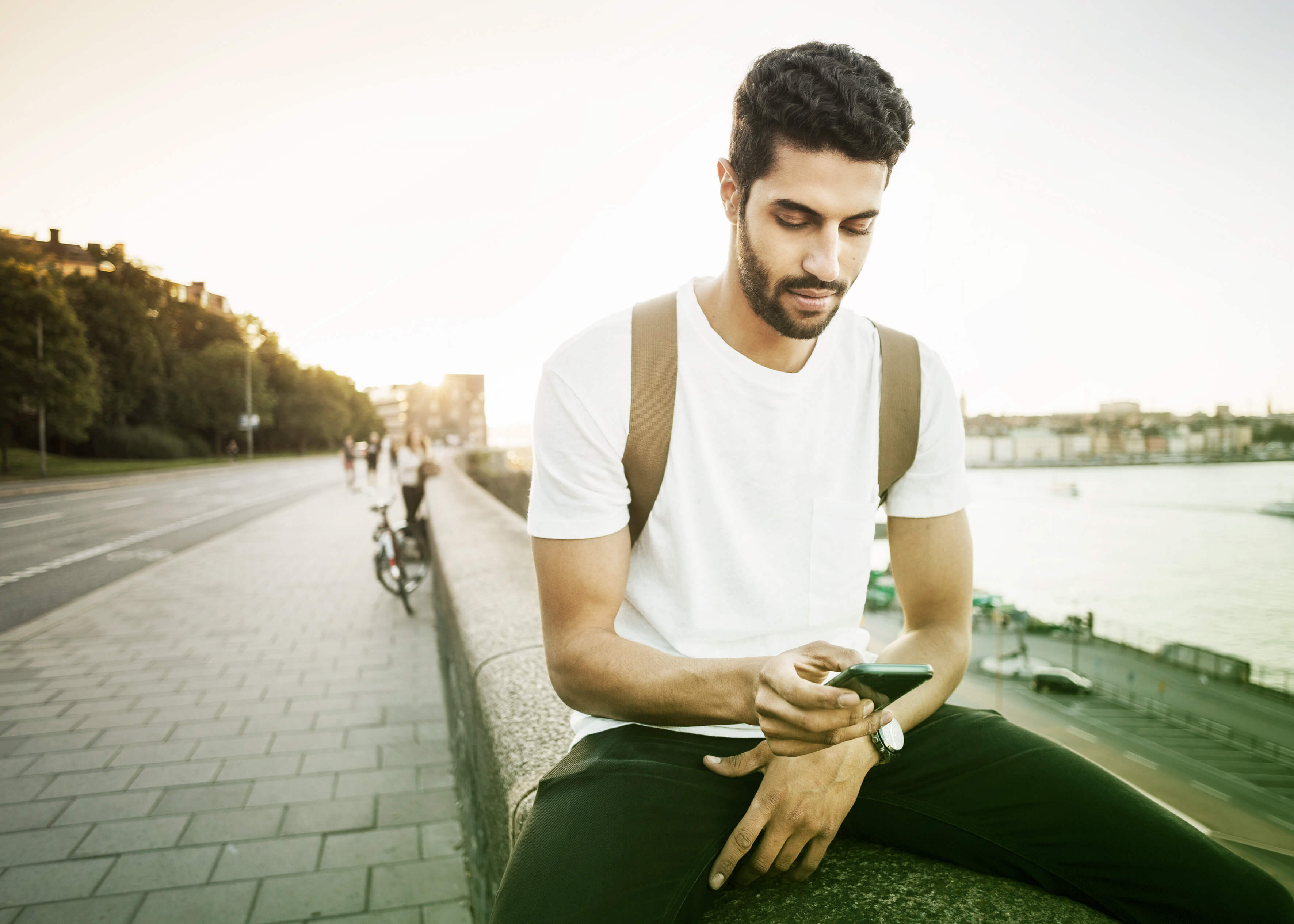 En man sitter på mur och tittar på Kivra i sin telefon