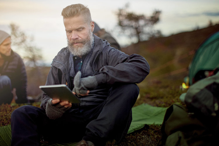 A man is out in the wilderness looking at his tablet.