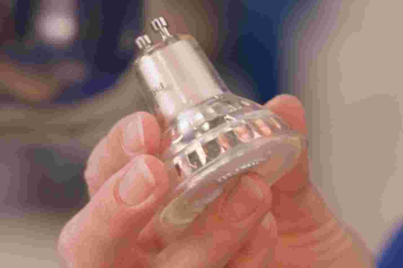Een hand houdt een LED spotje vast met GU10 fitting tegen een onscherpe achtergrond.