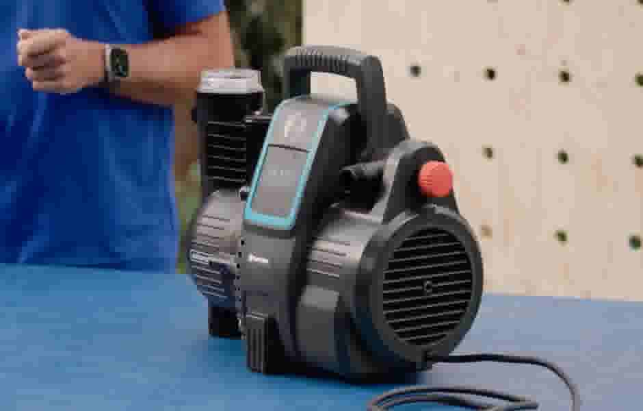 Zwart-blauwe Hydrofoorpomp op een blauwe tafel met persoon in blauw shirt op de achtergrond naast een houten wand.