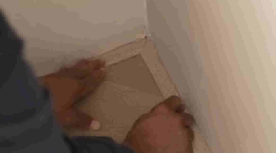 Handen plaatsen de plakstrip in een hoek van 90° tussen twee witte muren op de vloer