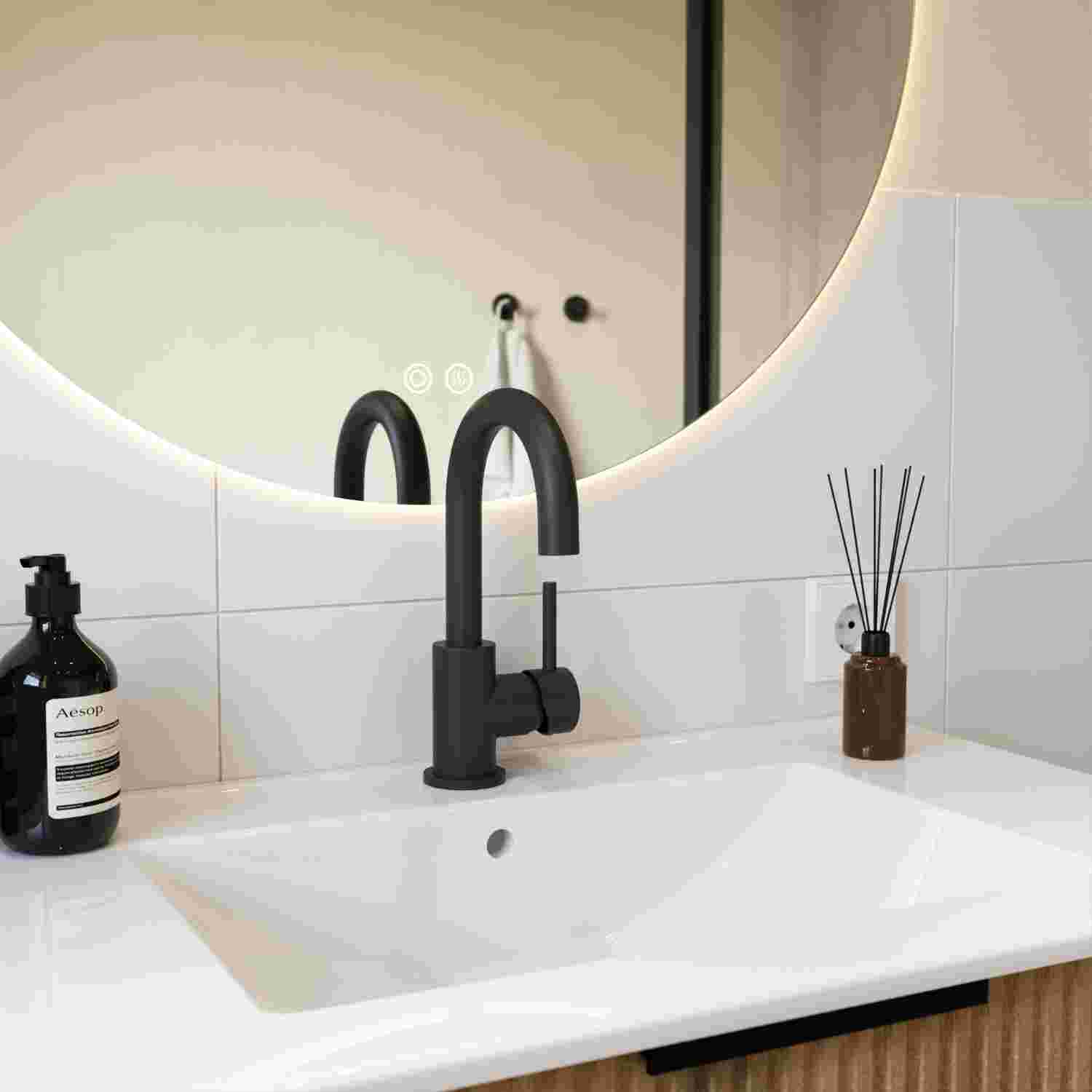 Een badkamer met zwarte kraan, witte wastafel en ronde verlichte spiegel