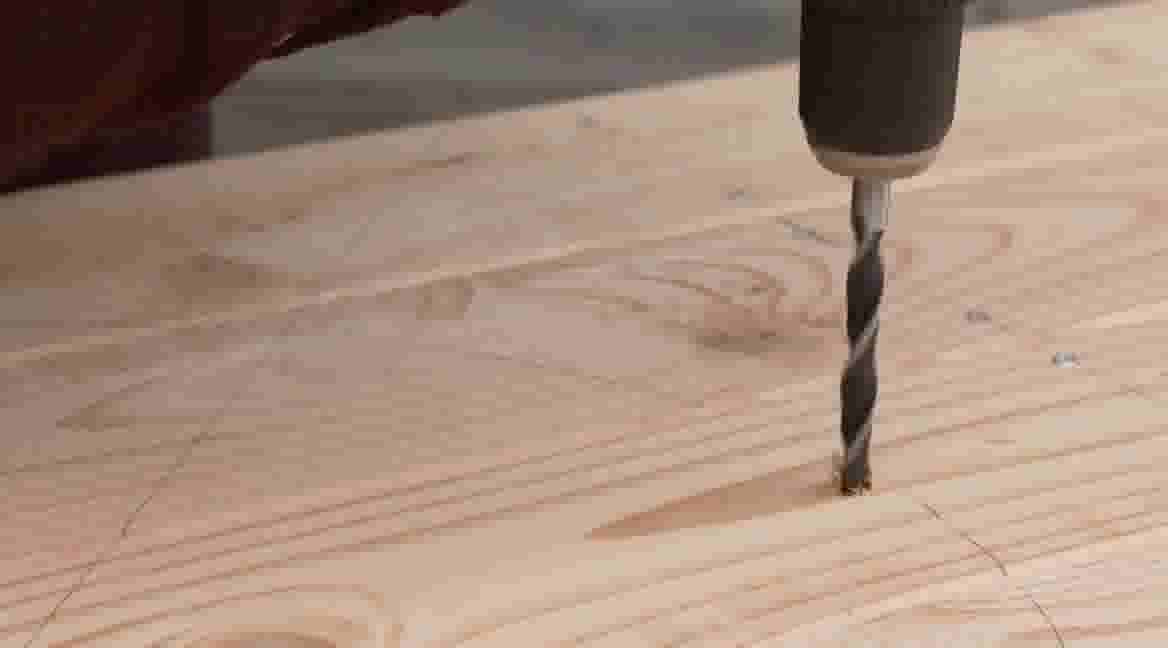 Een boorboor dringt in een houten plank met zichtbare houtnerven en potloodmarkeringen voor nauwkeurig boren.