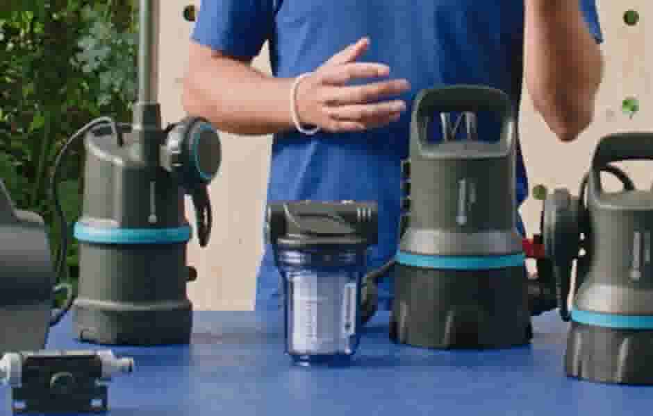 Persoon in blauw shirt demonstreert verschillende waterpompen met grijze behuizing en blauwe accenten op een blauwe tafel.