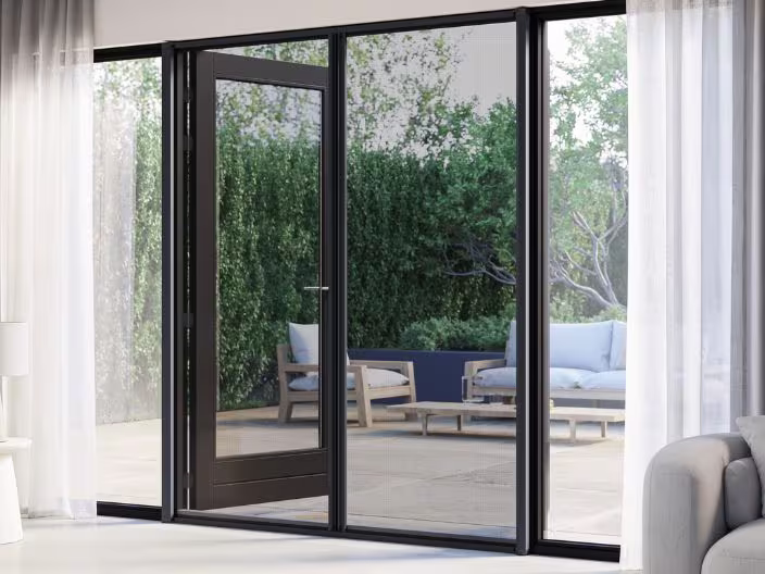 Openslaande glazen deuren met horren die uitkijken op een terras met loungemeubilair en groene hagen op de achtergrond.