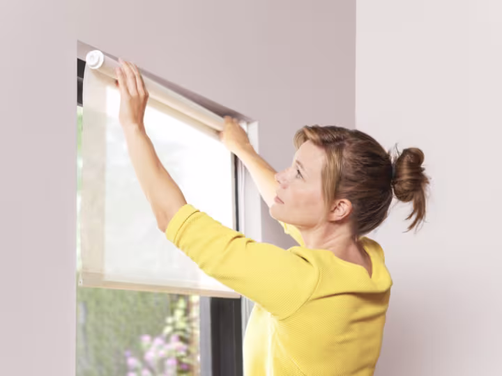 Vrouw monteert een licht beige rolgordijn voor een raam in een modern interieur.