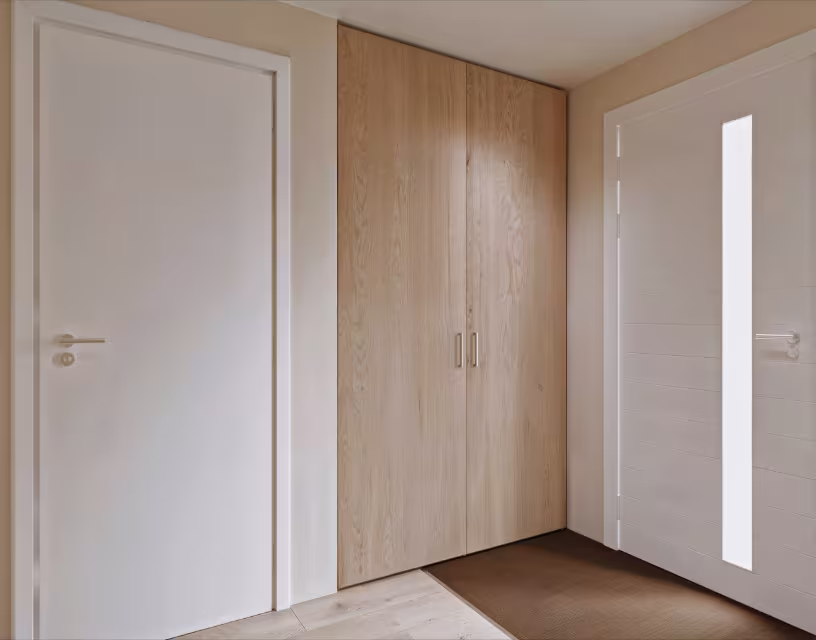 Moderne hal met witte deuren en grote houten inbouwkast met twee deuren en metalen handgrepen tegen beige muur.