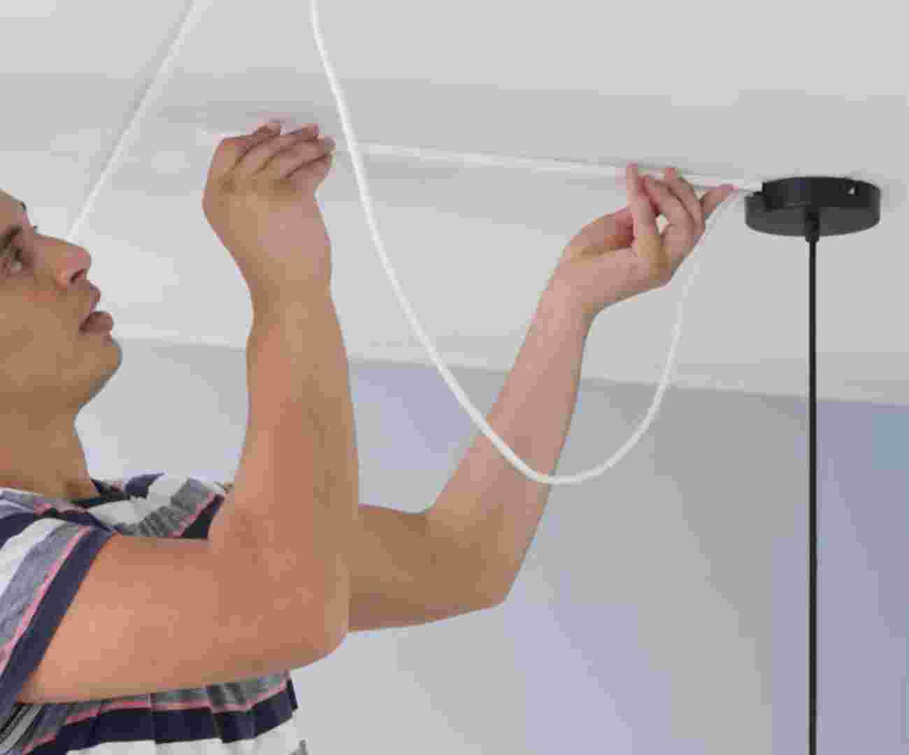 Een persoon die een kabelgootje op het plafond plakt