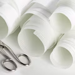 Meerdere opgerolde witte glasvezelbehangrollen naast een metalen schaar op een witte achtergrond.