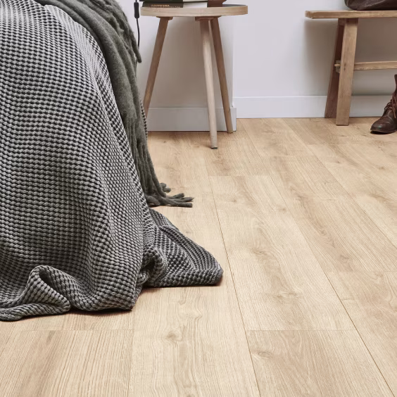 Lichte houten vloer met grijze deken, houten kruk en schoenen in moderne slaapkamer met witte muur.