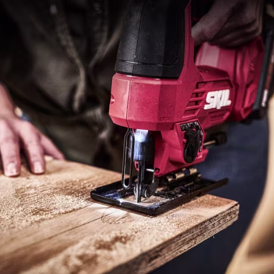 Persoon zaagt een houten plank met een rode SKIL decoupeerzaag. De hand houdt het hout vast terwijl zaagsel vrijkomt.