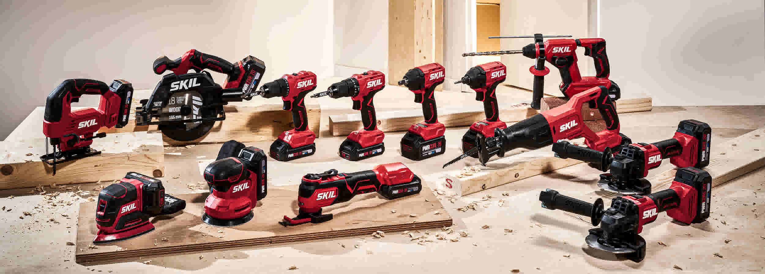 Collectie rode en zwarte SKIL elektrische gereedschappen uitgestald op houten werkblad met zaagsel.