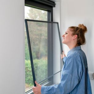 Persoon in blauw overhemd installeert een hor voor een raam met uitzicht op groen landschap.