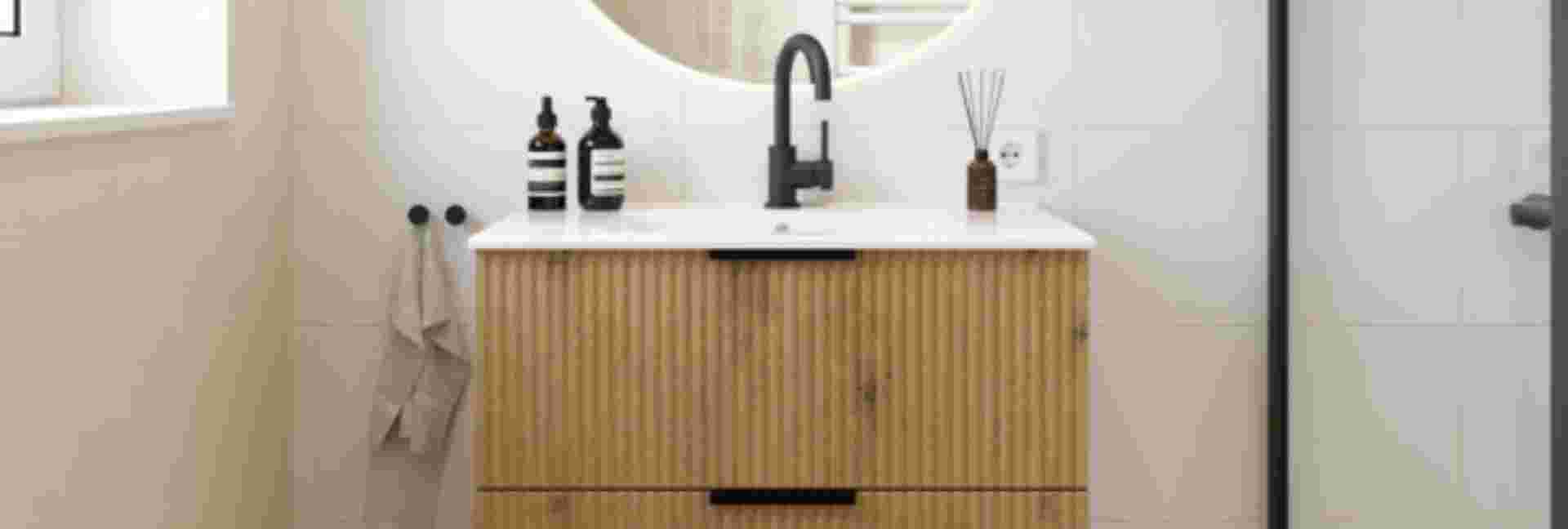 Moderne badkamer met houten wastafelmeubel, zwarte kraan, ronde spiegel en decoratieve flesjes op een wit aanrechtblad.