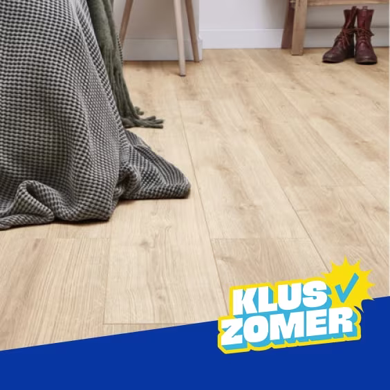 Lichte houten laminaatvloer in een kamer met een groene deken en bruine laarzen op de achtergrond. Logo Kluszomer zichtbaar.