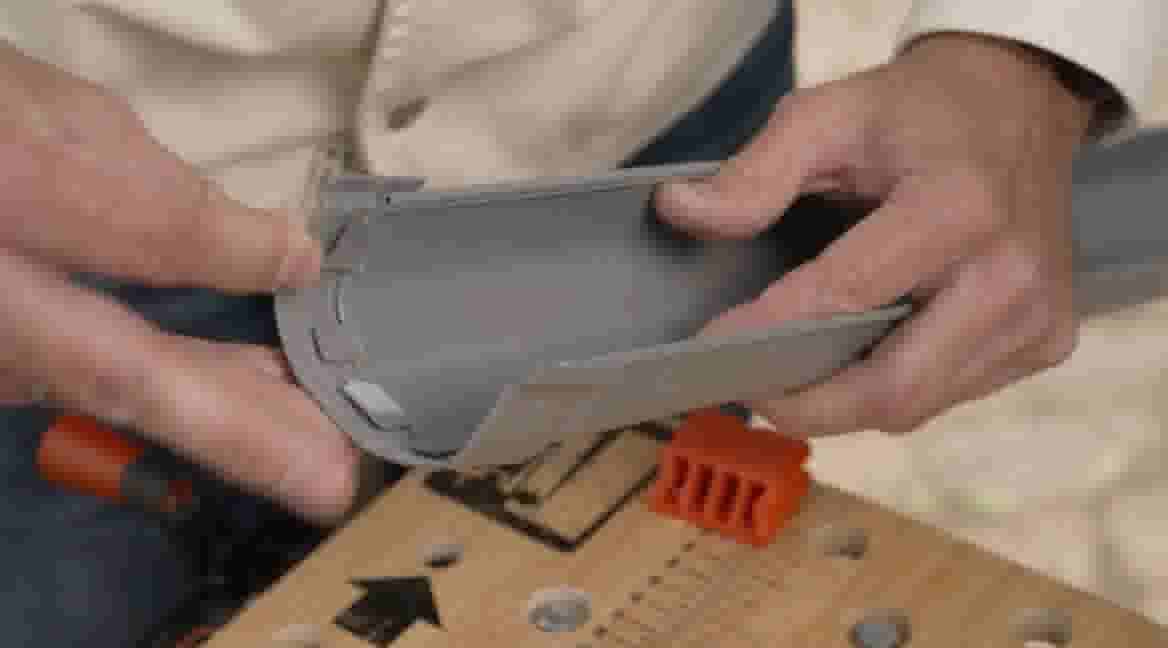 Handen installeren een grijs pvc-buisverbindingsstuk op een werkbank met oranje gereedschap en montage-instructies.