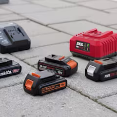 Verschillende oplaadbare lithium-ion batterijen en een oplader van verschillende merken op een betegelde ondergrond.