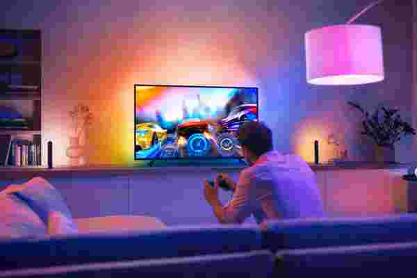 Persoon speelt racegame op tv in sfeervolle woonkamer met Philips Hue verlichting