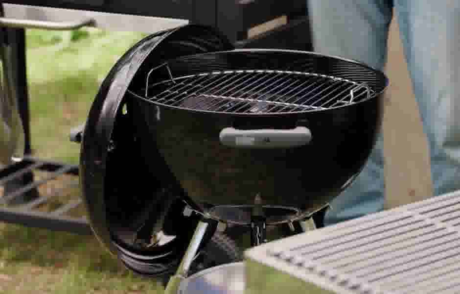 Zwarte Weber kogel barbecue met geopend deksel, klaar voor gebruik, geplaatst op gras in een buitenomgeving.