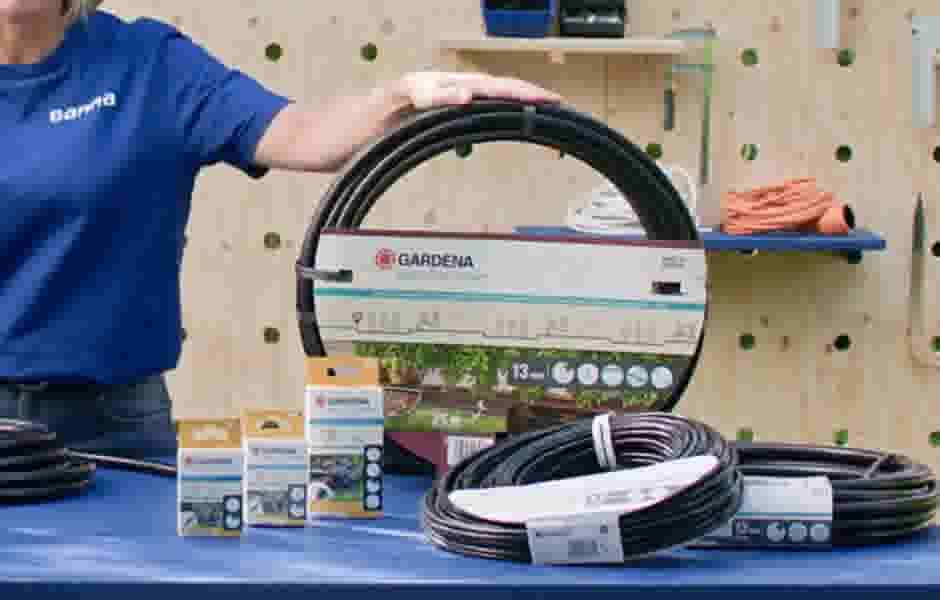 Persoon in blauw GAMMA shirt toont Gardena Micro-Drip irrigatiesysteem met slangen en accessoires op een werkbank.