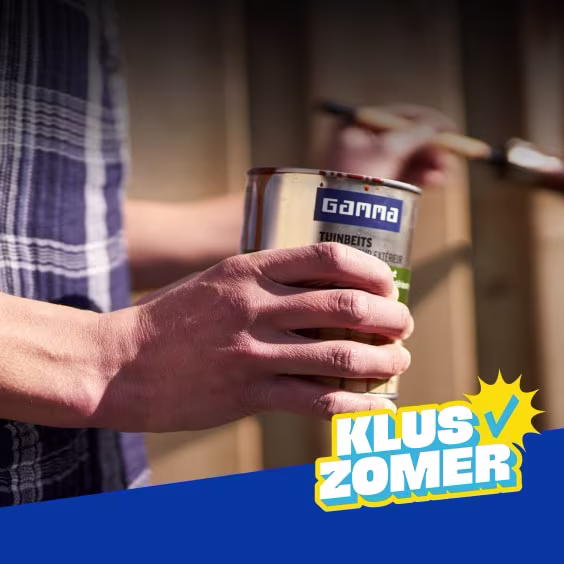 Persoon houdt een blik Gamma tuinbeits vast en schildert een houten schutting met een kwast. Logo 'Kluszomer' rechtsonder.