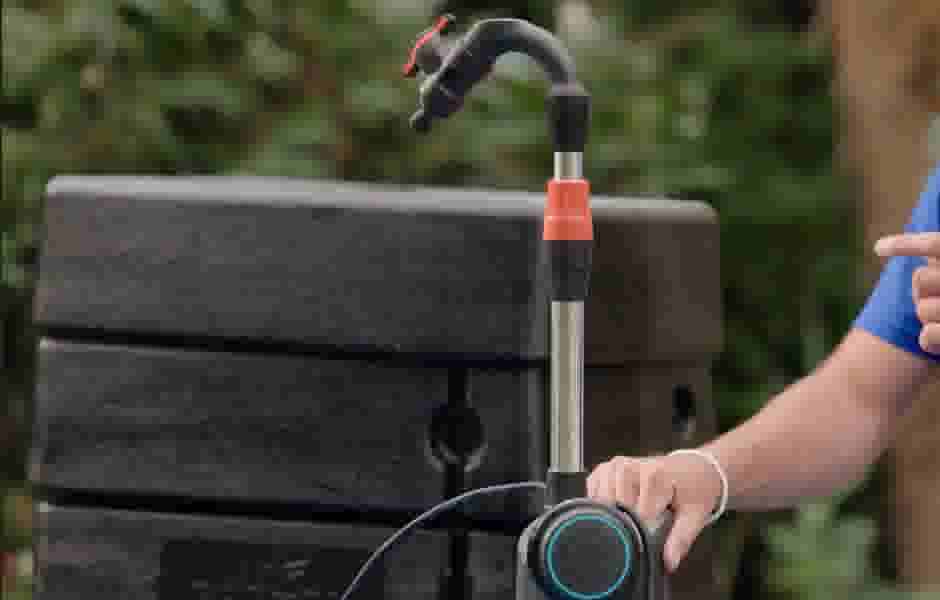 Waterkraan met rode hendel bevestigd aan een zwarte regenton, een hand bedient de pomp met blauwe ring.