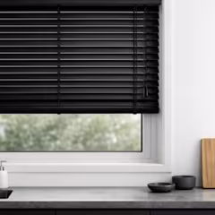 Zwarte horizontale jaloezie voor een raam in een keuken, met een aanrecht en kleine zwarte schaaltjes ernaast.