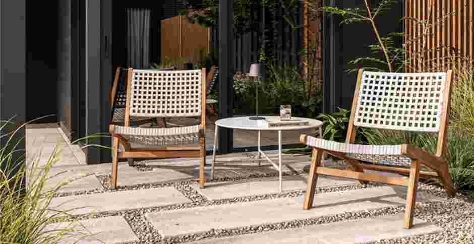 Modern terras met twee witte gevlochten stoelen en ronde tafel, omringd door groen en houten schutting in een stijlvolle tuin.