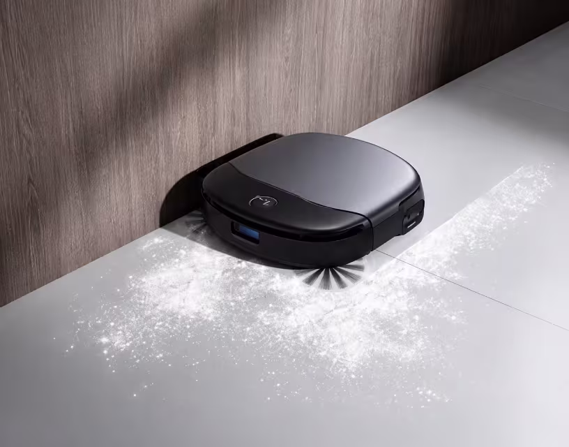 Zwarte robotstofzuiger reinigt witte vloer met zichtbaar stof, tegen houten wand met donkere hoek.