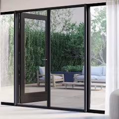 Moderne zwarte hordeuren die openen naar een terras met loungemeubilair, omgeven door groene planten.