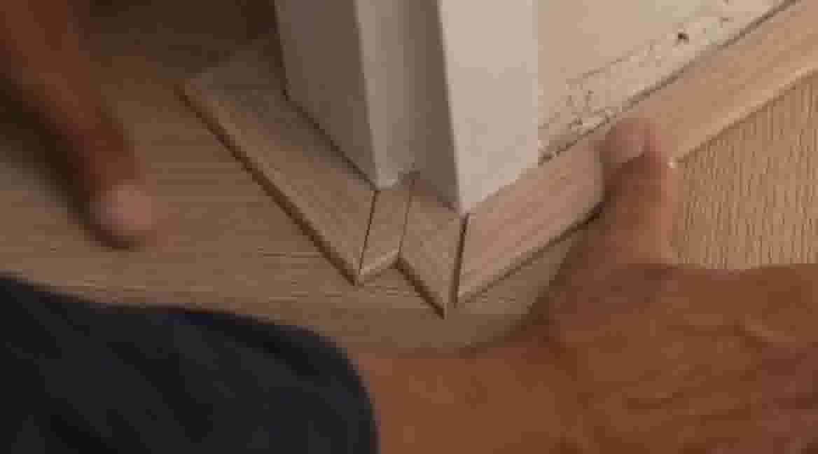 Handen plaatsen houten plinten op de vloer bij een deurpost, met nauwkeurig gesneden hoekverbindingen.