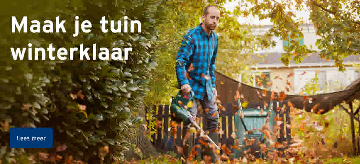 Man in blauw geruit overhemd blaast herfstbladeren in tuin met bladblazer onder groene bomen