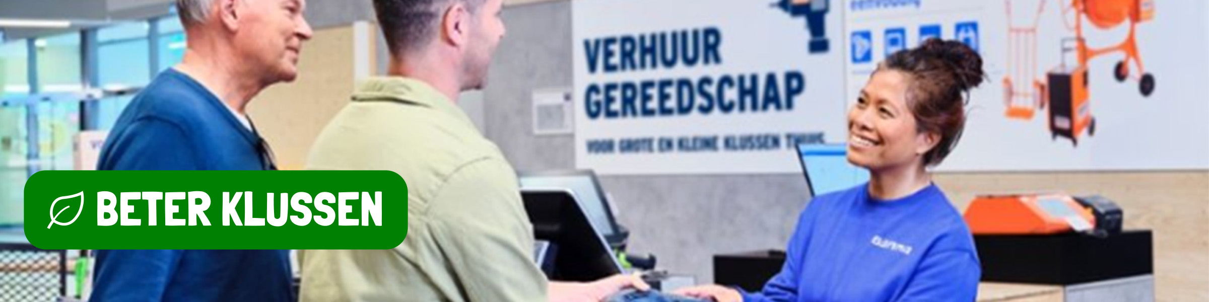 GAMMA medewerker in blauwe trui helpt klanten bij gereedschapsverhuur, met op de achtergrond een "VERHUUR GEREEDSCHAP" bord.
