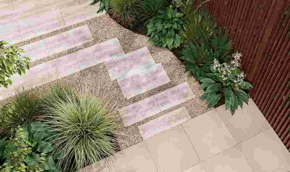 Moderne tuintrap met betonnen treden op grind, omringd door siergras en groene planten naast een houten schutting.