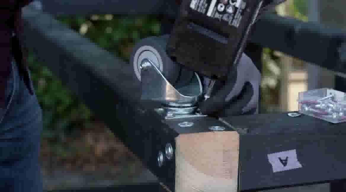 Elektrisch gereedschap snijdt door metaal op een houten werkbank, met handschoenen voor veiligheid.