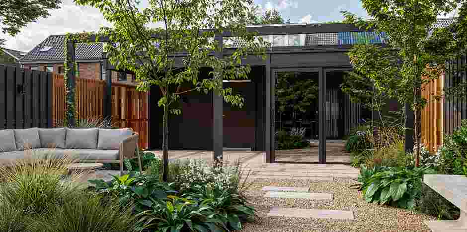 Moderne tuinhuis met glazen schuifdeuren, omringd door weelderige planten en een comfortabele loungebank in een stijlvolle tuin.