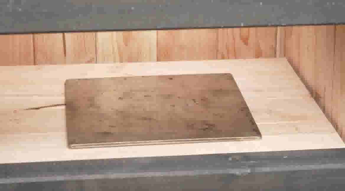 Een gebruikte metalen bakplaat ligt op een houten oppervlak met lichthouten wandpanelen op de achtergrond.