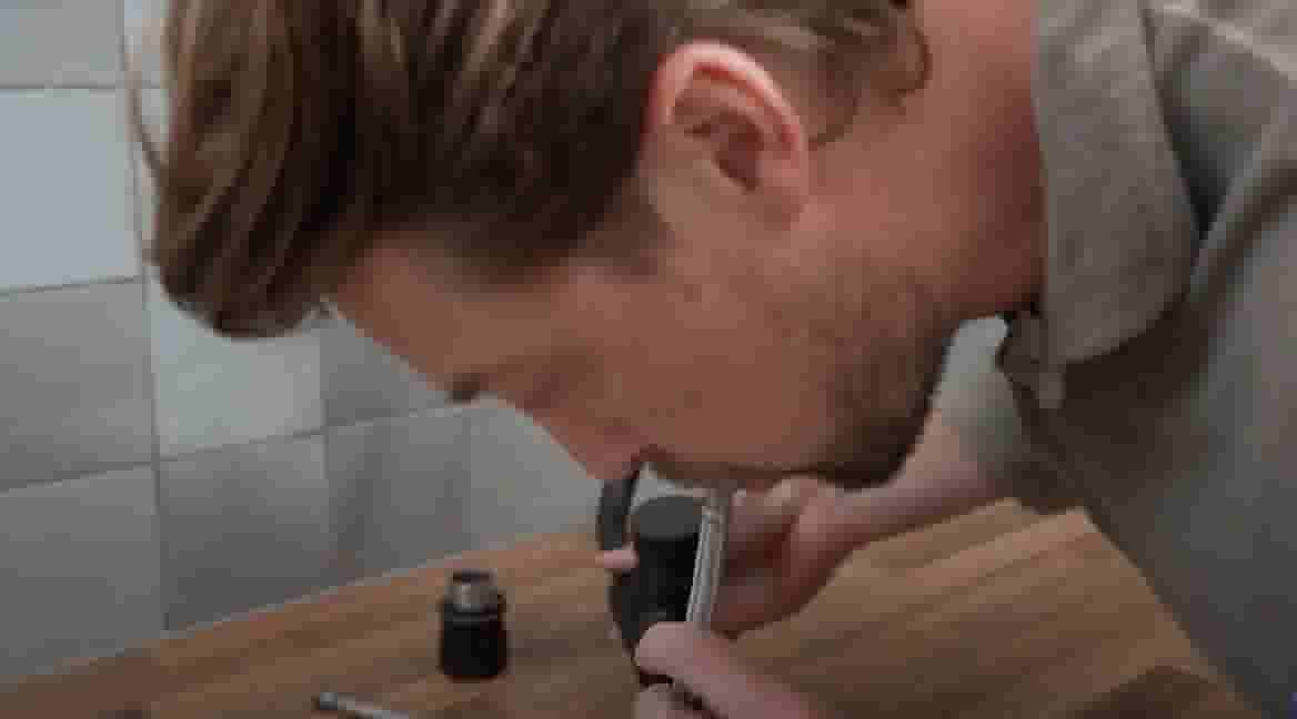 Persoon buigt voorover en blaast door de flexibele slang om te controleren of die op de goede plek zit. 