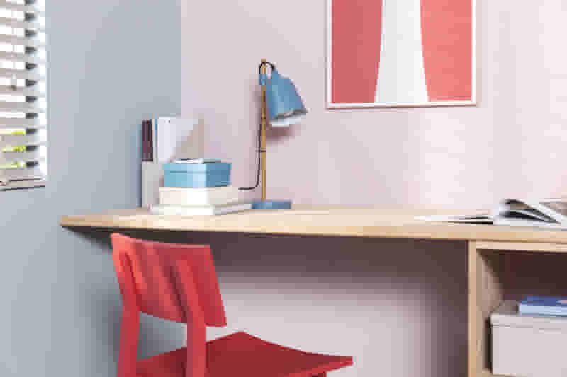 Een houten bureau die in de hoek staat met daarop wat spullen zoals een bureaulamp en wat boeken.