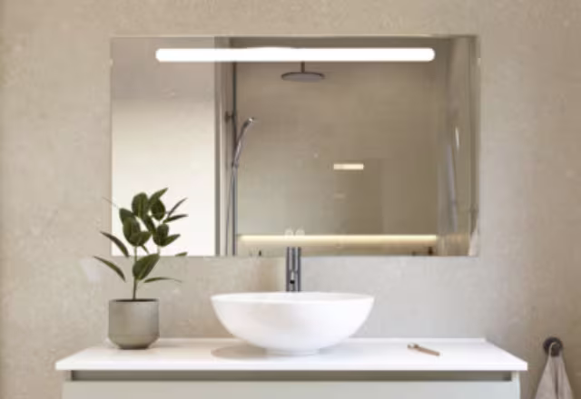 Moderne badkamer met witte waskom op wit meubel, verlichte spiegel en groene plant in pot voor een frisse uitstraling.