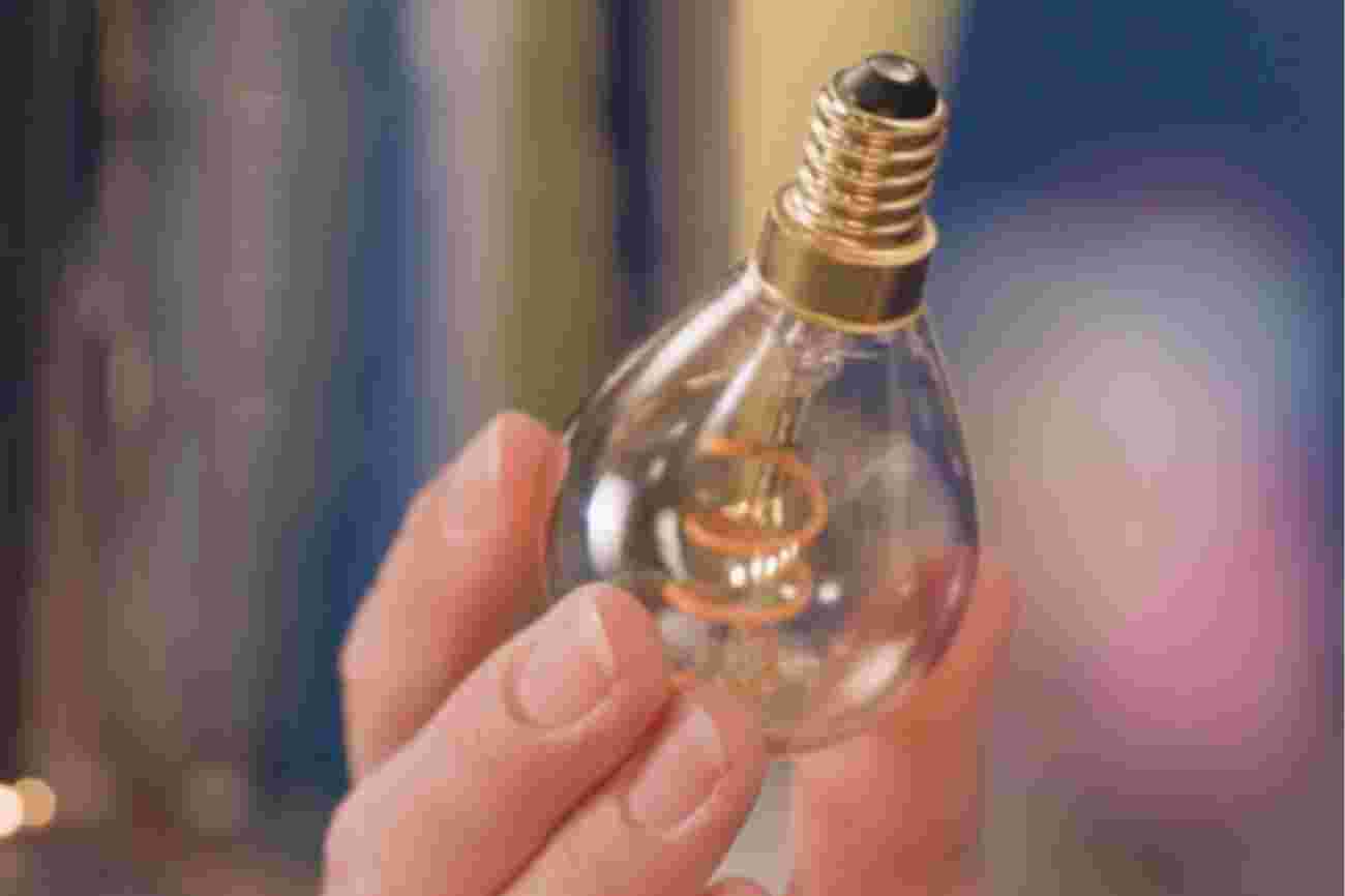 Een hand houdt een Filament LED lamp vast met E14 schroeffitting tegen een onscherpe achtergrond.
