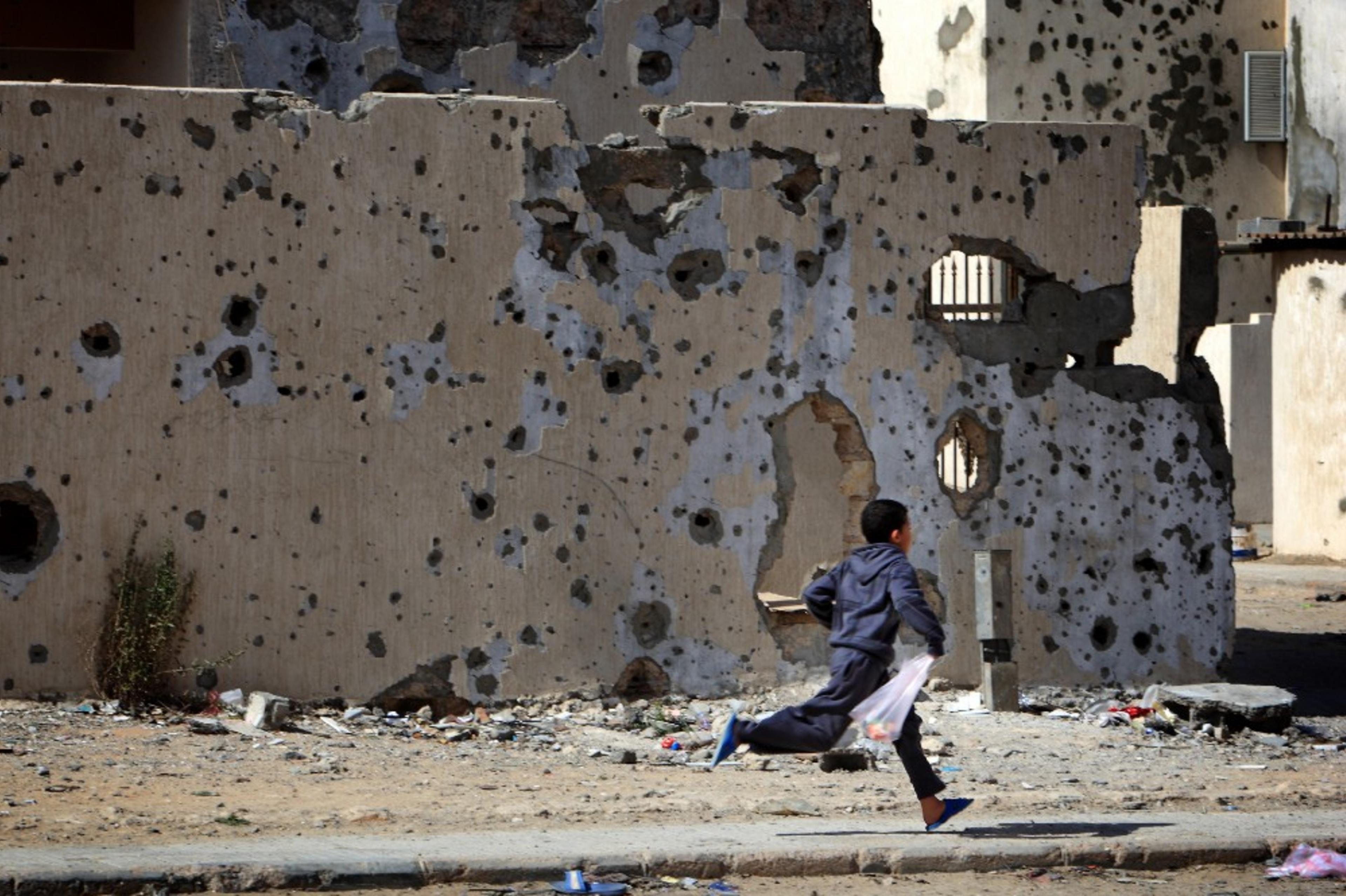 A child in Libya runs past damaged buildings on his way home from shopping