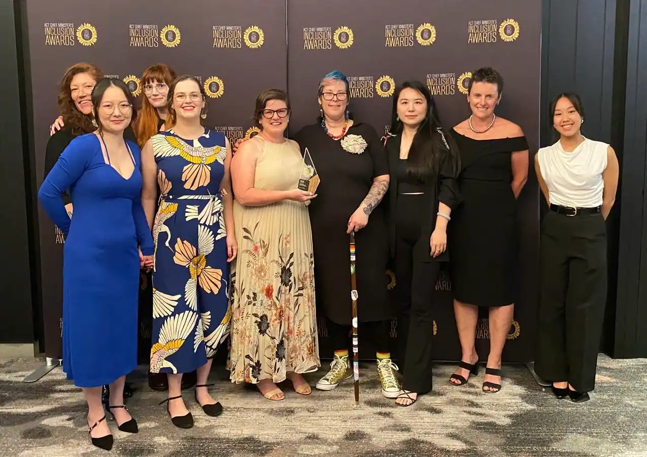 Some of the project advisory group for Safer Me Safer You, and some of the SMSY and SHFPACT team holding a glass award and smiling at the camera.