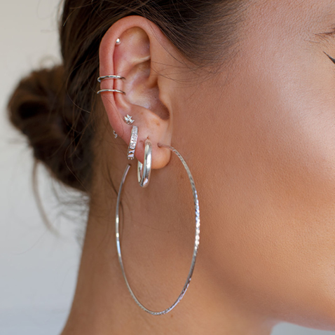 femme portant 7 boucles d'oreilles superposées en argent, créoles et puces